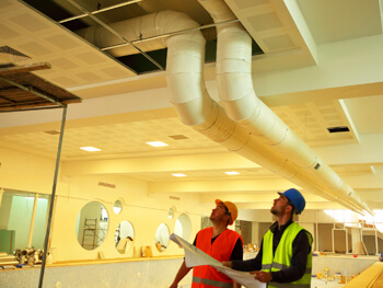 Two technicians wearing safety gear reviewing HVAC designs at a client facility